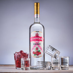 1 liter Fles Petrovskaia Cherry Premium kersen Vodka omringd door shotglaasjes, verse kersen en een kersencocktail