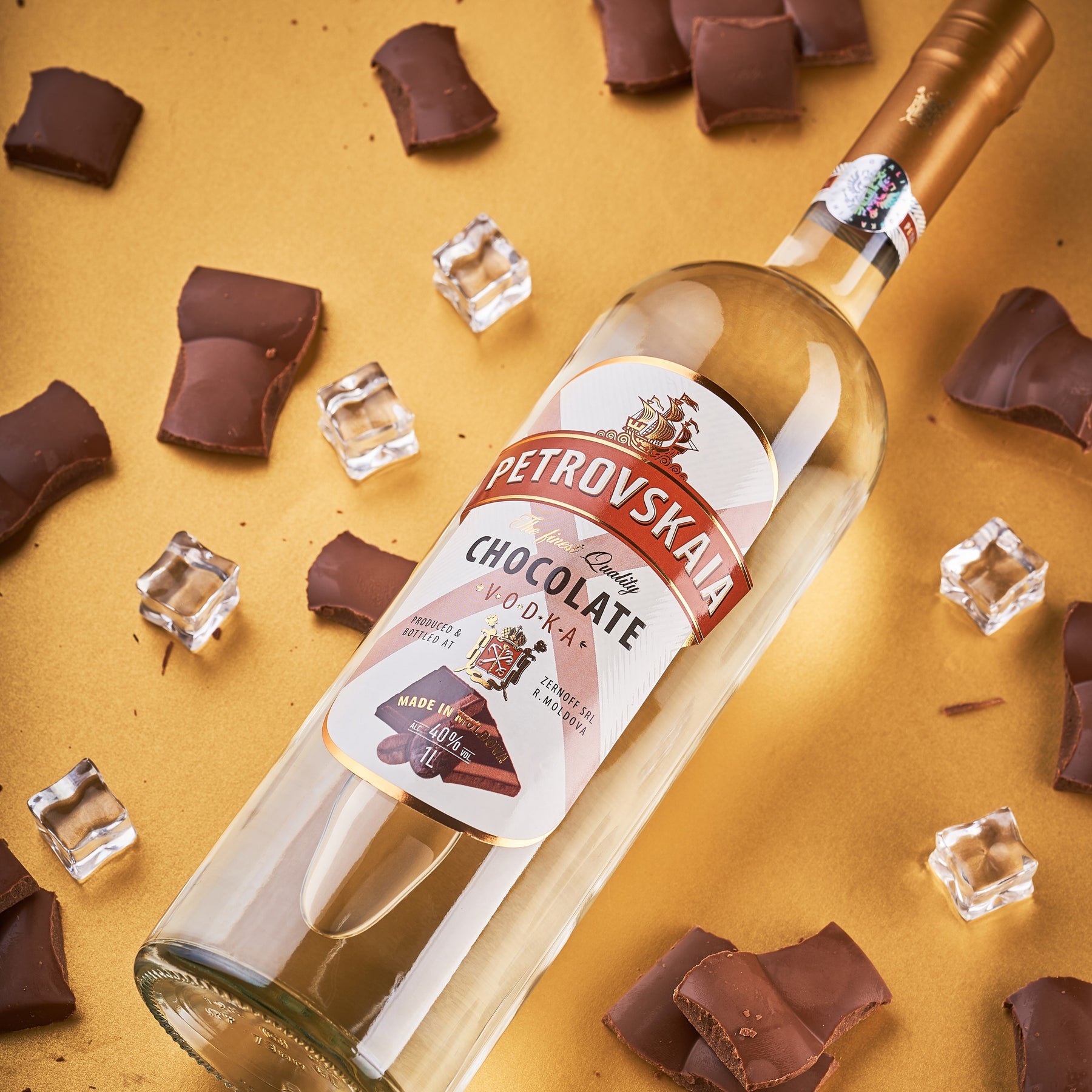 Petrovskaia Chocolate Vodka fles liggend op een gouden achtergrond met stukjes chocolade en ijsblokjes, kwaliteit chocolade vodka.