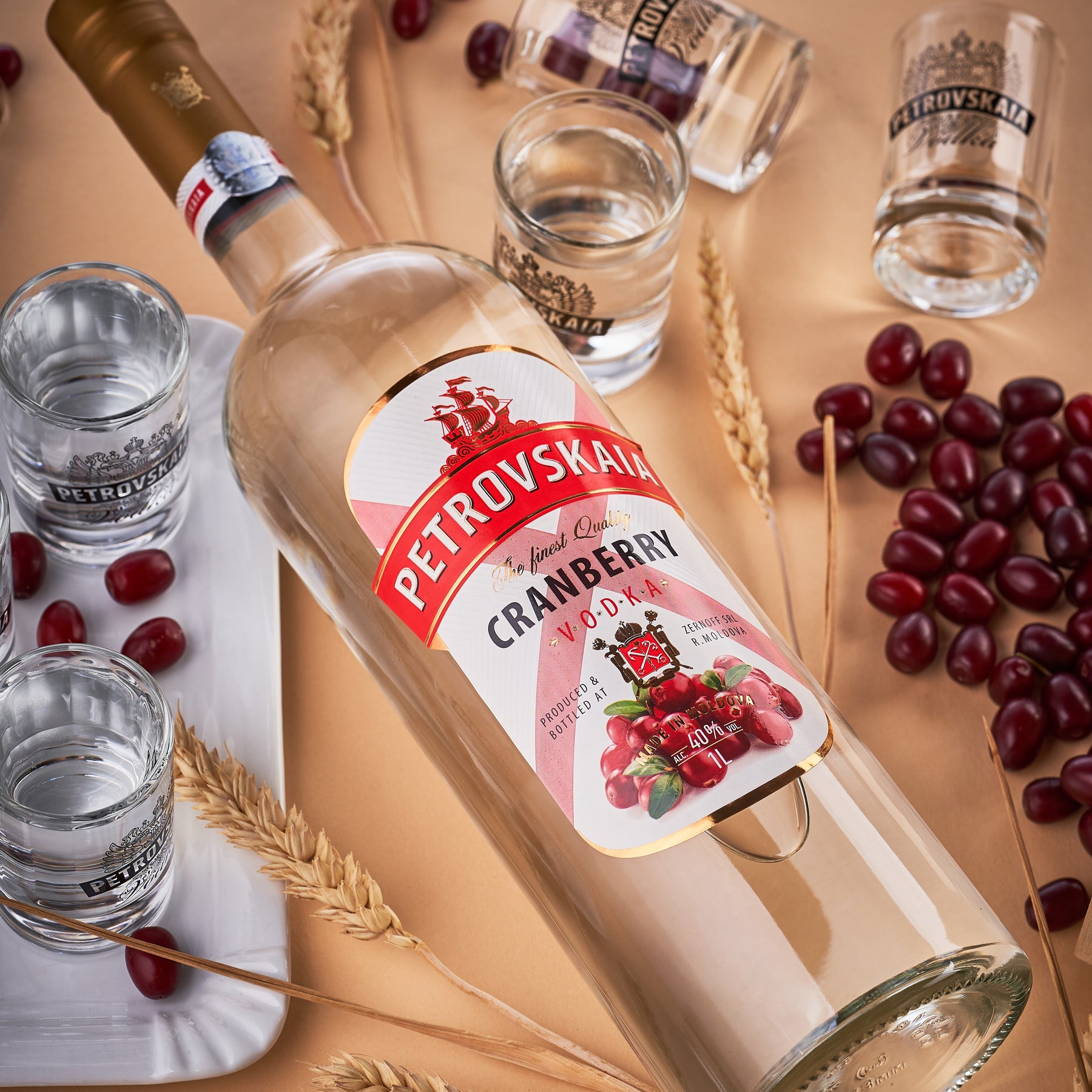 Petrovskaia Cranberry Vodka fles schuin liggend tussen verse granen, cranberries en veenbessen, luxe en premium drank. 