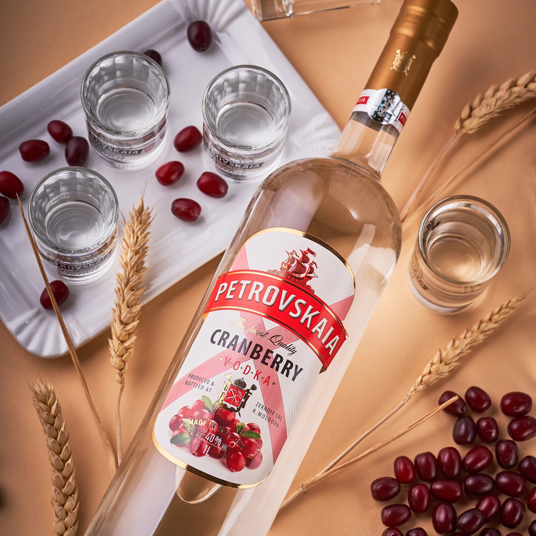 Petrovskaia Cranberry Vodka 1 Liter fles schuin liggend tussen verse cranberries en veenbessen op warme beige-oranje achtergrond, luxe cocktaildrank.