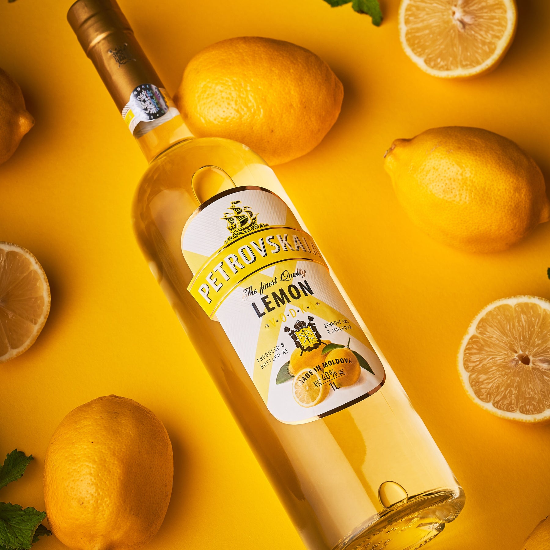 Petrovskaia Lemon Vodka 1 liter fles schuin liggend op een gele achtergrond met hele en gesneden citroenen, hoogwaardige citroenwodka.