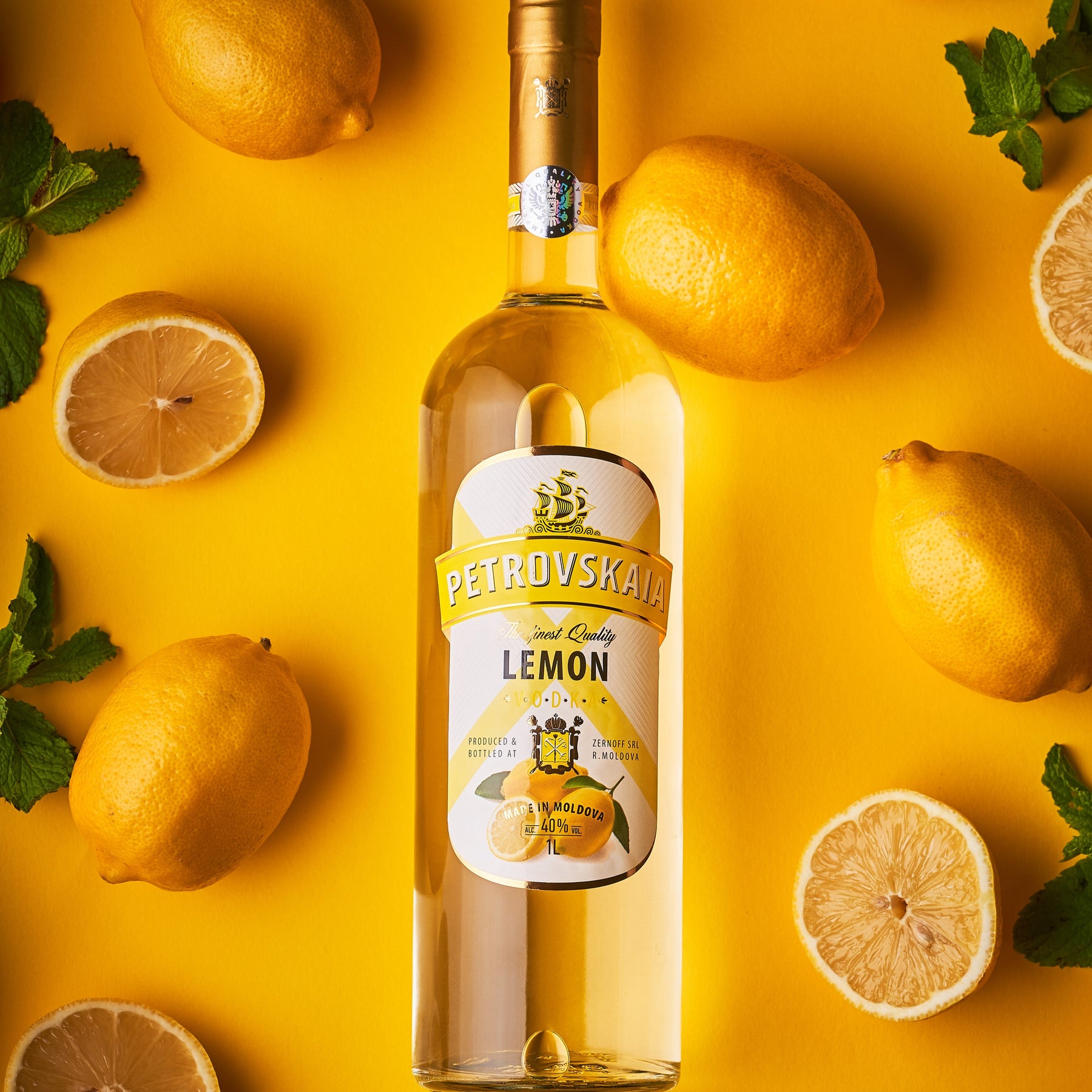 Petrovskaia Lemon Vodka 1 liter fles verticaal liggend op een gele achtergrond met hele en gesneden citroenen, premium verfrissende citroenwodka.