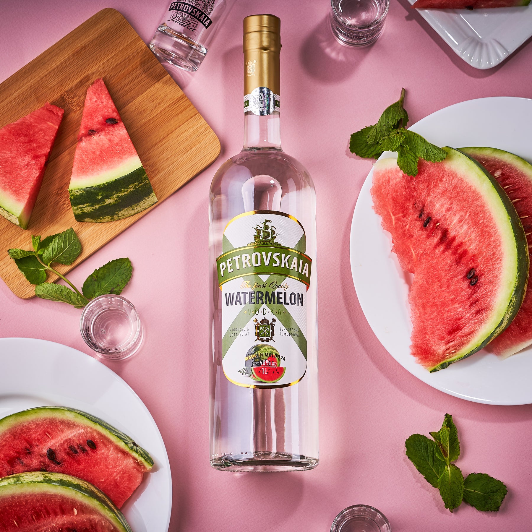 Petrovskaia Watermeloen Vodka 1 liter fles in omringd door een halve watermeloen, 2 stukken gesneden watermeloen op een snijplank, munt en een shotglaasje, luxe watermeloenwodka.